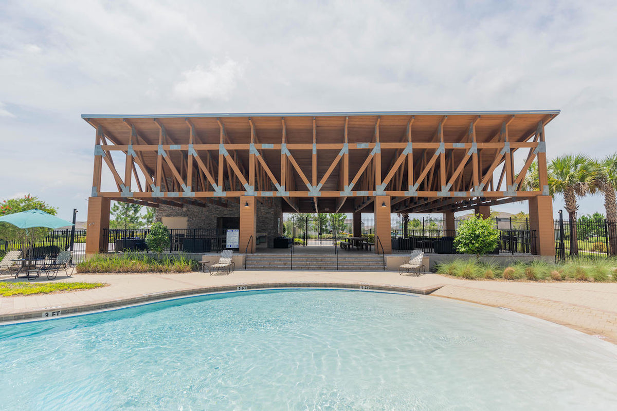 The Copperspring Amenity Center's open-air timber pavilion seen across the pool, its trusses joined with galvanized steel plates