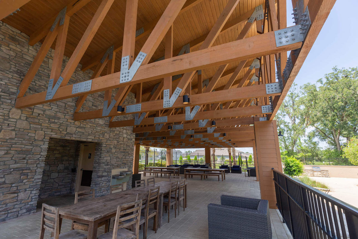 The pavilion's stone fireplace and dining tables under timber trusses joined with galvanized plates