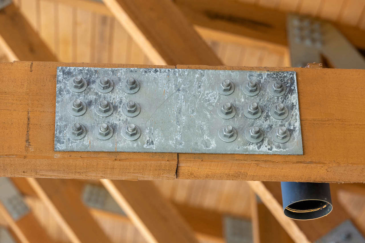 A galvanized steel splice plate bolted across a joint in a timber chord