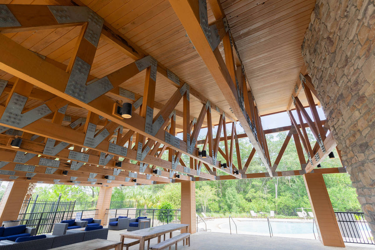 The length of the pavilion under its trusses, with lounge seating and the pool beyond