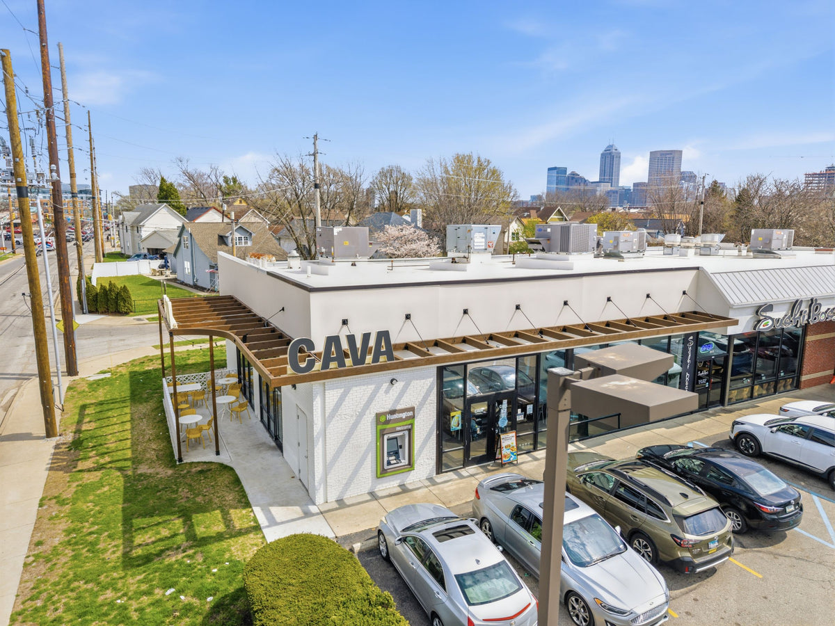 Aerial view of the Indianapolis CAVA, its timber awning and patio pergola hung on steel tie rods, with the downtown skyline behind