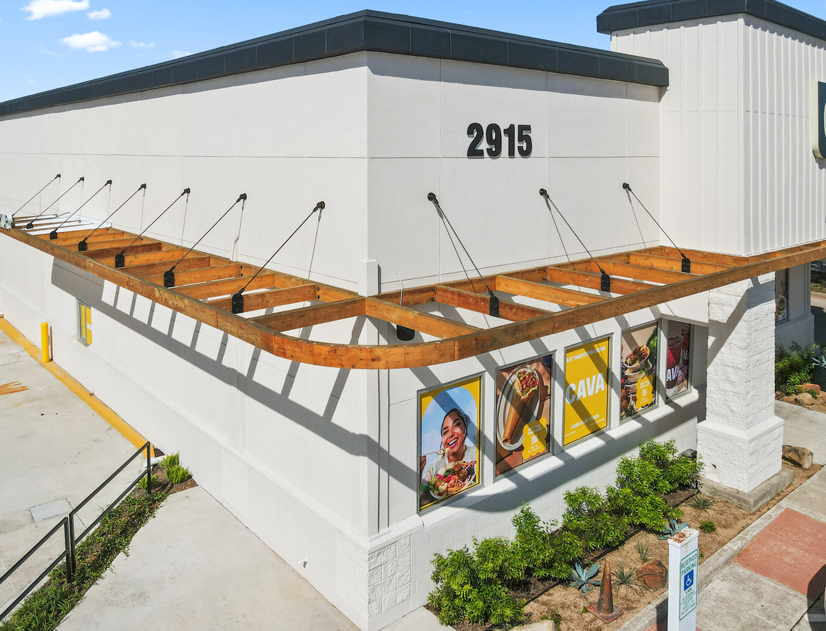 Timber awning along the League City CAVA, each beam held from the wall by a black steel tie rod and bracket