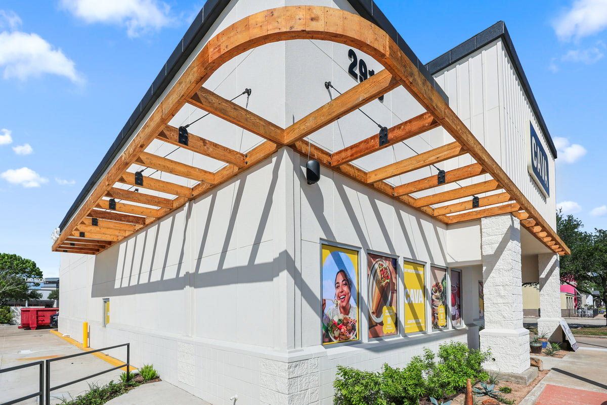 Looking up at the curved timber awning at the League City CAVA, with black steel tie rods anchored to the wall above