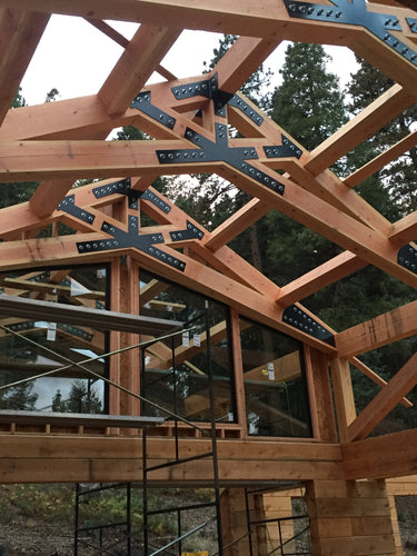 Timber frame trusses joined with black steel gusset plates, under construction among pine trees