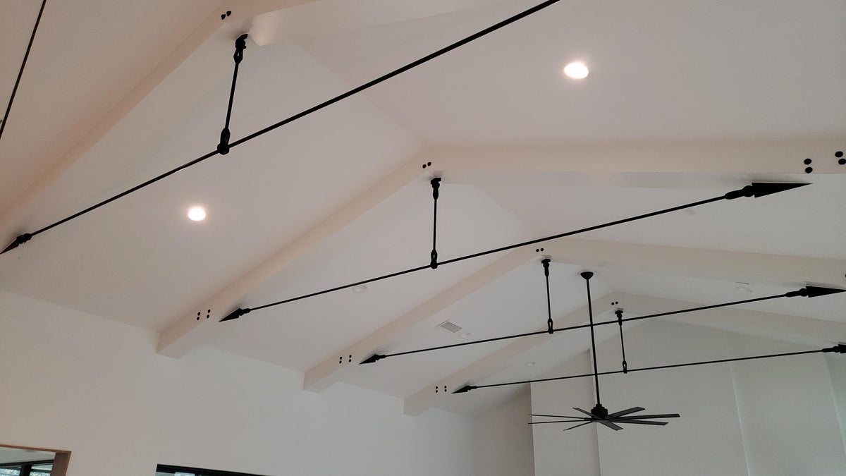 Black tie rods with vertical hangers spanning white exposed rafters in a vaulted ceiling